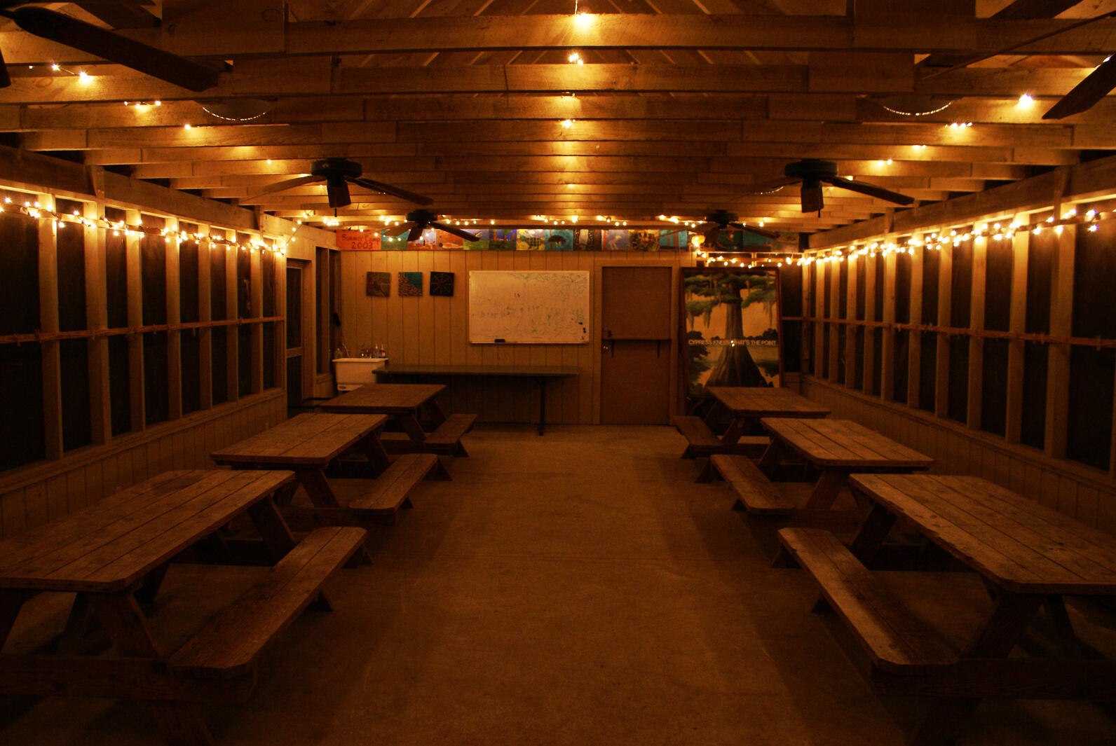 A view from inside Beidler's outdoor classroom, only now at night. Lights illuminate the ceiling, creating a cozy appearance and possibly distracting from the possibility of nocturnal wildlife lurking beyond in the woods.